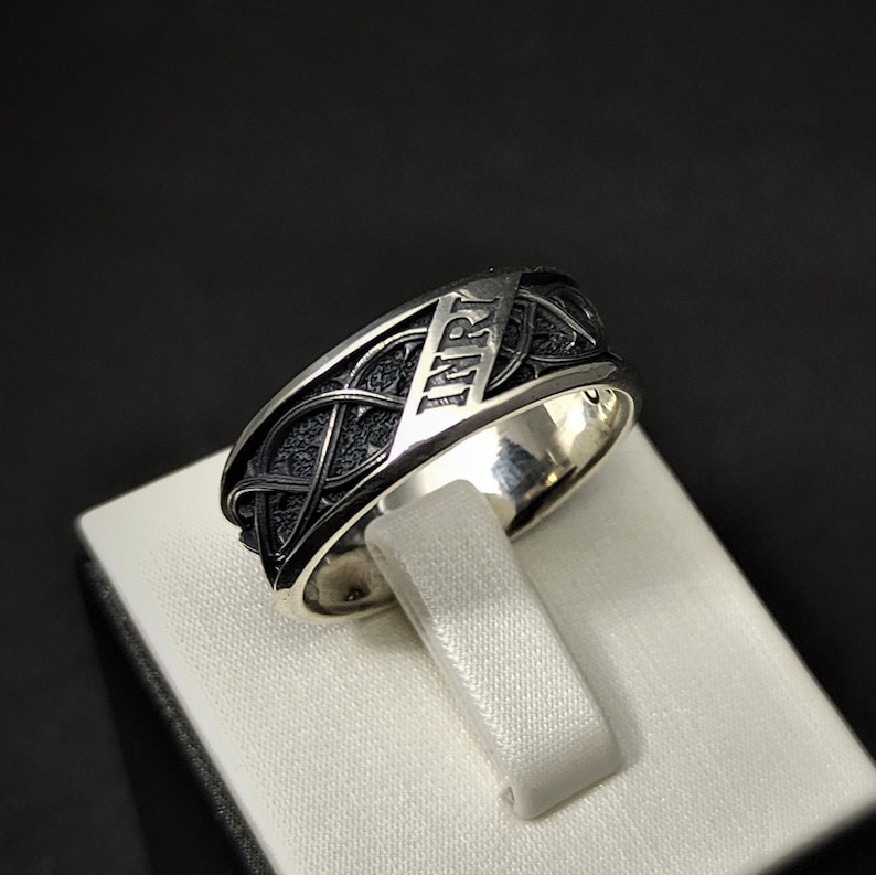May include: A silver ring featuring a black Celtic knot design with the word "Mirt" engraved on the band.