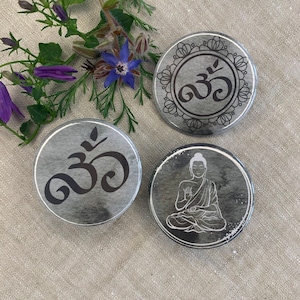 Könnte beinhalten: Drei runde graue und weiße Knöpfe mit schwarzen Designs. Ein Knopf zeigt ein stilisiertes Om-Symbol mit einem dekorativen Rand. Ein weiterer Knopf zeigt ein stilisiertes Om-Symbol. Der dritte Knopf zeigt eine weiße Silhouette eines meditierenden Buddha.