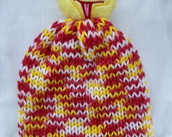May include: A red, yellow, and white knitted hat with a yellow bird character on top. The bird has a pink tongue and black eyes.