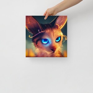 May include: Square canvas art featuring a digital illustration of a cat with large, glowing blue eyes. The cat has tan and brown fur with glowing gold accents around the ears and face. The artwork is held by a hand against a white background.