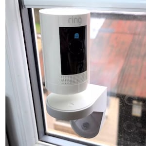 May include: A white Ring security camera mounted on a window with the word "ring" printed on the front of the camera.
