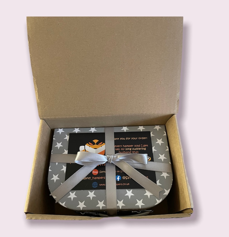 May include: A gift box with a gray and white star pattern, tied with a silver ribbon. The box contains a card with text and a cartoon fox. The box is inside a brown cardboard box.