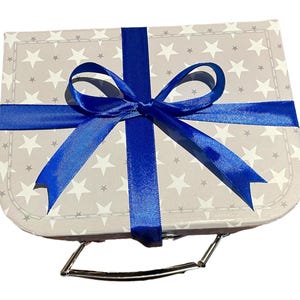 May include: A small, grey gift box patterned with white stars, tied with a bright blue ribbon and bow. The box has a silver handle, suitable for various occasions.