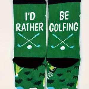 May include: Green socks with the text "I'D RATHER GOLFING" in white. The socks feature crossed golf clubs and a golf ball in light blue. The top of the socks are black.