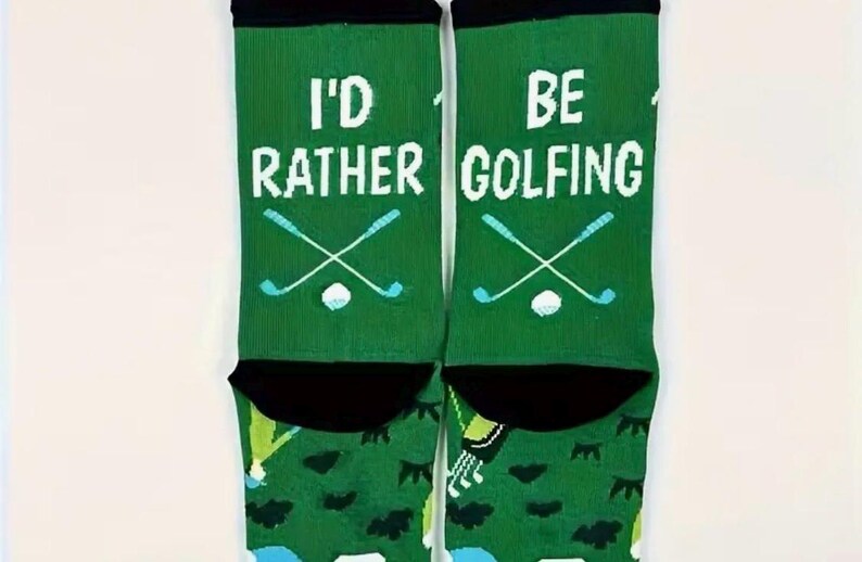 May include: Green socks with the text "I'D RATHER GOLFING" in white. The socks feature crossed golf clubs and a golf ball in light blue. The top of the socks are black.
