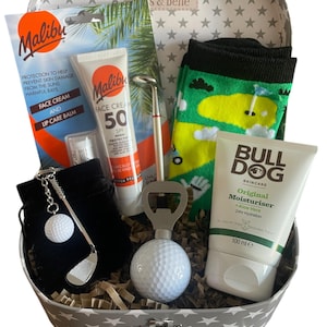 May include: A golf-themed gift set in a star-patterned case. Contents include sunscreen, lip balm, a golf ball keyring, a golf club pen, a golf ball bottle opener, golf socks, and Bulldog moisturiser. The moisturiser is 100 ml.