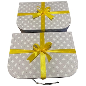 May include: Two grey gift boxes patterned with white stars, tied with bright yellow ribbons and bows. The boxes are rectangular with rounded corners, and the bows are centred on top.