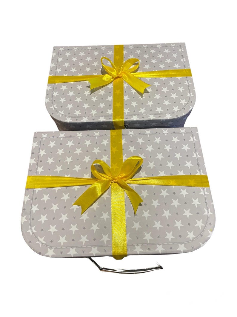 May include: Two grey gift boxes patterned with white stars, tied with bright yellow ribbons and bows. The boxes are rectangular with rounded corners, and the bows are centred on top.