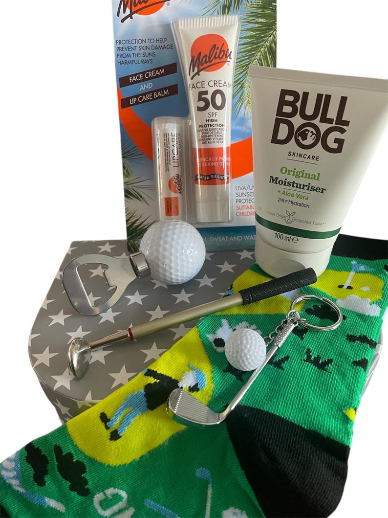 May include: A gift set with golf-themed items, including a green sock, sunscreen, lip balm, and moisturiser. It features a golf ball, a golf club keyring, and a golf ball marker. The box has a star pattern.