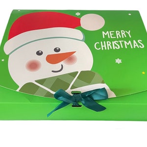 Puede incluir: Caja de regalo verde con un dise&ntilde;o de mu&ntilde;eco de nieve y el texto "Feliz Navidad". La caja tiene una cinta verde.