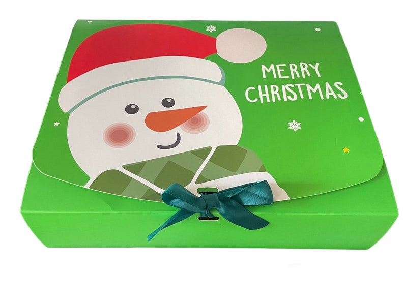 Puede incluir: Caja de regalo verde con un dise&ntilde;o de mu&ntilde;eco de nieve y el texto "Feliz Navidad". La caja tiene una cinta verde.