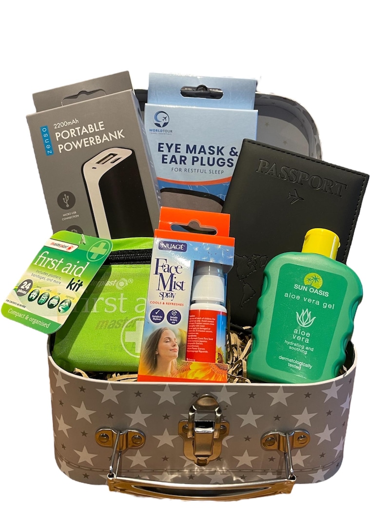 May include: A travel-themed gift basket filled with essentials. Includes a portable power bank, eye mask and ear plugs, a passport, aloe vera gel, a first aid kit, and face mist spray. The basket is gray with white stars.
