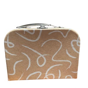 May include: A small, tan-colored suitcase with a silver handle and clasp. The suitcase is decorated with white, abstract, swirling lines. The design is repeated across the front and sides of the case.