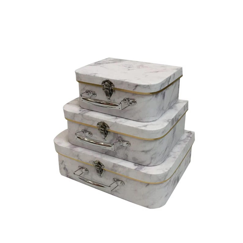 May include: Three decorative storage boxes with a marble effect pattern, stacked on top of each other. Each box has a silver handle and clasp, with a gold trim. The boxes are rectangular with rounded corners, in descending size.