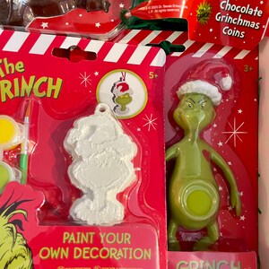 Puede incluir: Un kit de manualidades de Navidad con el Grinch. El kit incluye un adorno de Grinch para pintar, una figura de Grinch y monedas de chocolate Grinchmas. El embalaje es rojo y blanco con las palabras "The Grinch" y "Pinta tu propia decoraci&oacute;n".