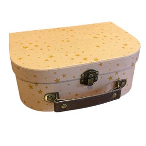 May include: A pink and gold star-patterned suitcase with a brown handle and metal clasp. The suitcase has a rounded top and a rectangular base. The stars are gold and scattered across the pink surface. The handle is brown and attached with metal hardware.