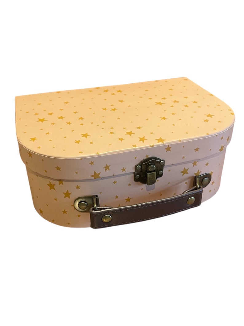 May include: A pink and gold star-patterned suitcase with a brown handle and metal clasp. The suitcase has a rounded top and a rectangular base. The stars are gold and scattered across the pink surface. The handle is brown and attached with metal hardware.