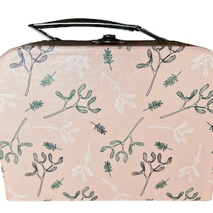 May include: A blush-colored suitcase with a black handle and clasp. The suitcase is decorated with a repeating pattern of mistletoe and leaf illustrations in shades of green and white. The suitcase has a rounded top and bottom.