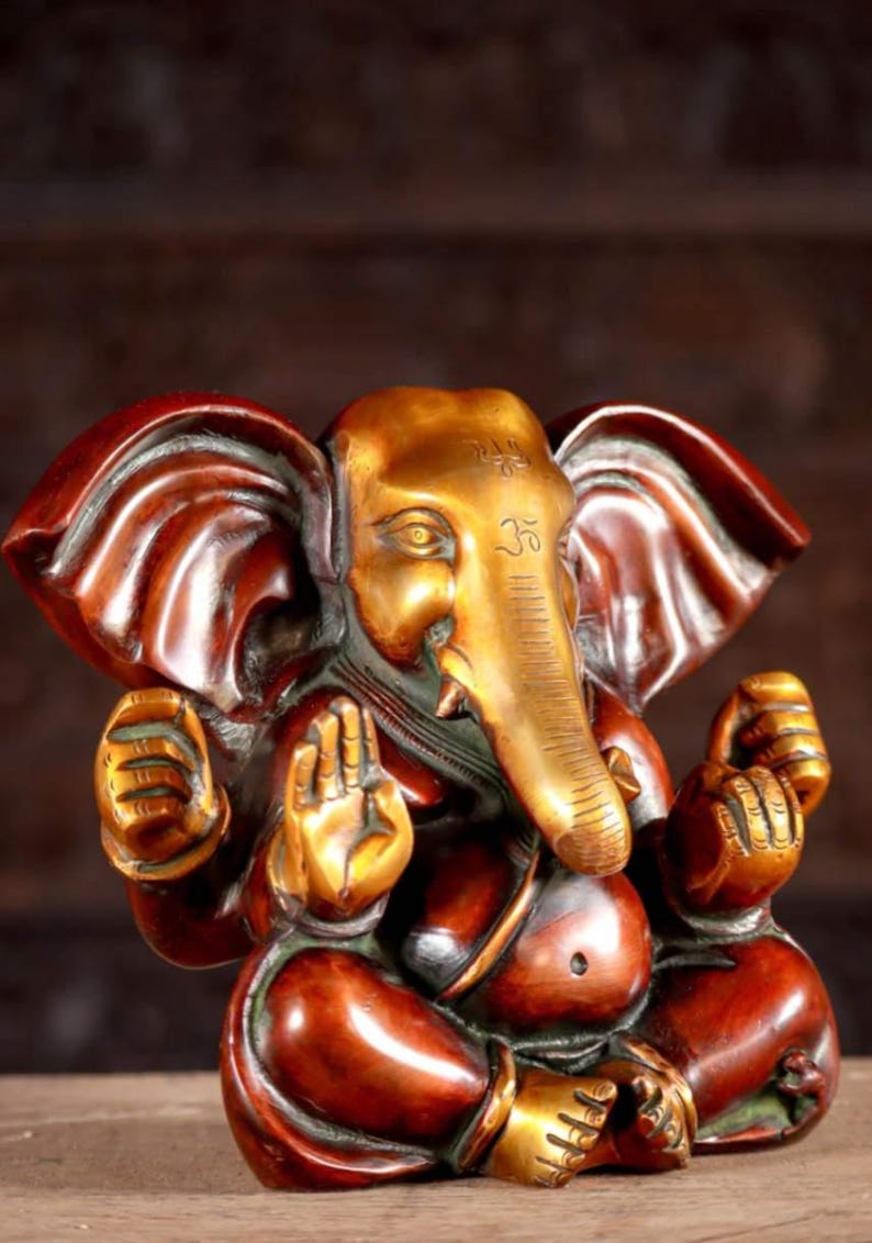 Puede incluir: Una estatua de bronce dorada y roja de Ganesha, el dios hind&uacute; de los comienzos, la sabidur&iacute;a y la prosperidad. La estatua representa a Ganesha sentado con la trompa levantada y las manos en un gesto mudra. La estatua est&aacute; intrincadamente detallada y tiene un dise&ntilde;o tradicional.