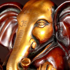 Puede incluir: Una estatua de metal dorado y marr&oacute;n de Ganesha, el dios hind&uacute; de la sabidur&iacute;a y la prosperidad. La estatua presenta detalles intrincados, que incluyen una gran trompa de elefante, un solo colmillo y una corona.