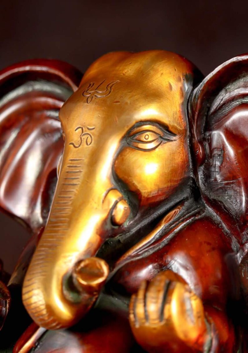 Puede incluir: Una estatua de metal dorado y marr&oacute;n de Ganesha, el dios hind&uacute; de la sabidur&iacute;a y la prosperidad. La estatua presenta detalles intrincados, que incluyen una gran trompa de elefante, un solo colmillo y una corona.