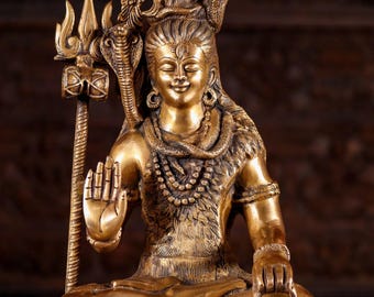 Puede incluir: Una estatua de bronce dorada de Shiva, una deidad hindú, sentado en una postura meditativa. Sostiene un tridente en su mano derecha y una olla pequeña en su mano izquierda. Está adornado con una serpiente alrededor de su cuello y una corona en su cabeza.