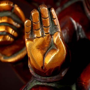 Puede incluir: Primer plano de una mano dorada con tallas detalladas, parte de una estatua m&aacute;s grande. La mano est&aacute; levantada con los dedos extendidos, lo que sugiere un gesto de bendici&oacute;n o protecci&oacute;n.