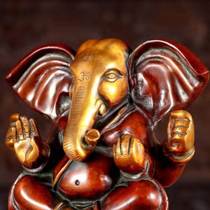 Puede incluir: Una estatua de bronce dorada y roja de Ganesha, el dios hind&uacute; de los comienzos, la sabidur&iacute;a y la prosperidad. La estatua representa a Ganesha sentado con la trompa levantada y las manos en un gesto mudra.