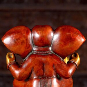 Puede incluir: Una estatua de Ganesha roja y dorada con un dise&ntilde;o detallado. La estatua est&aacute; sentada en una postura meditativa con las manos en mudra.