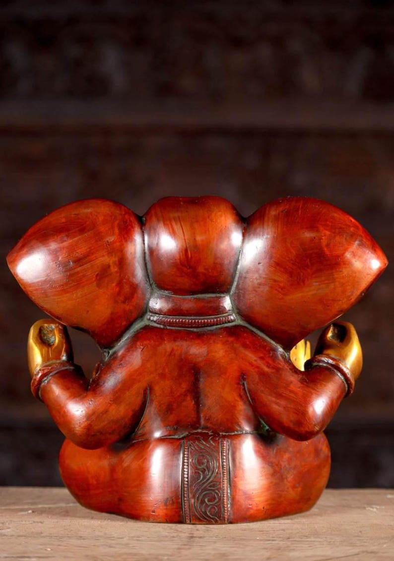 Puede incluir: Una estatua de Ganesha roja y dorada con un dise&ntilde;o detallado. La estatua est&aacute; sentada en una postura meditativa con las manos en mudra.