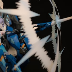 以下が含まれることがあります： 青い紙製のモデルは、長い紫色の髪を持つ女性アニメキャラクターで、青と白の衣装を着て、青い刃を持つ大きな白い武器を持っています。モデルは、武器を頭上に掲げたダイナミックなアクションポーズをとっています。モデルはGZpaperによって作られました。