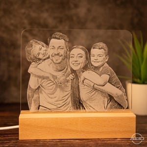 Peut inclure: Une base en bois avec un panneau en acrylique transparent repr&eacute;sentant une image grav&eacute;e en noir et blanc d'une famille de quatre personnes. La famille sourit et semble appr&eacute;cier la compagnie de chacun.