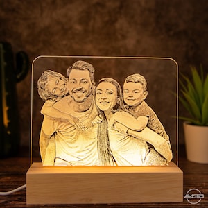 Peut inclure: Une veilleuse LED personnalis&eacute;e avec une base en bois. La lumi&egrave;re pr&eacute;sente un portrait de famille d'un homme, d'une femme et de deux enfants. L'image est grav&eacute;e dans le panneau acrylique et &eacute;clair&eacute;e par derri&egrave;re.