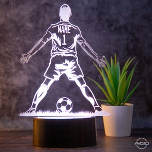 Könnte beinhalten: Eine weiße, 3D-gedruckte Nachtlampe in Form eines Fußballspielers mit dem Wort "NAME" und der Nummer "1" auf der Rückseite des Trikots. Der Spieler tritt einen Fußball.