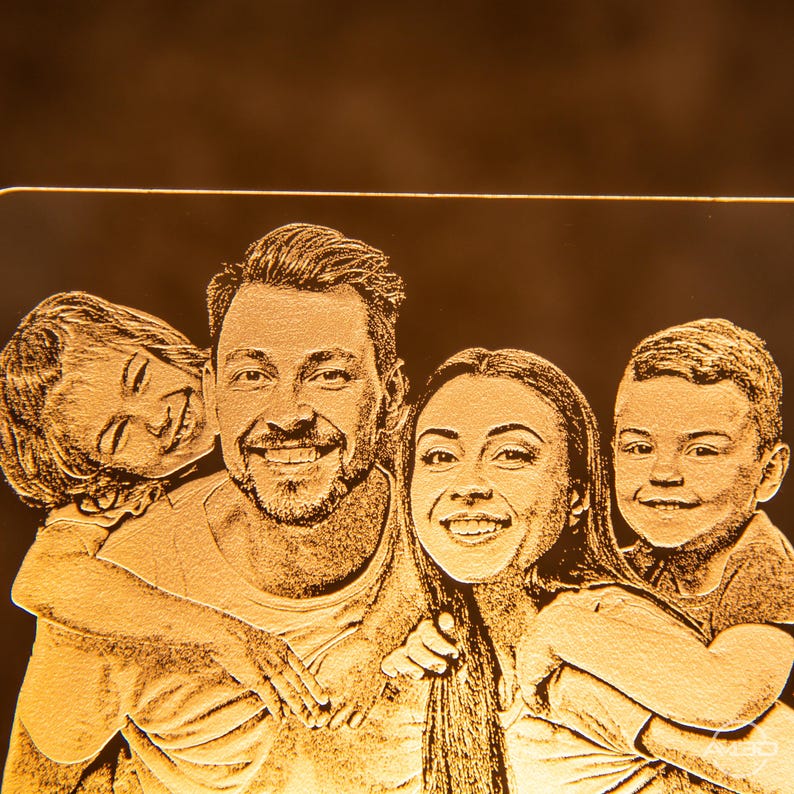 Peut inclure: Une image grav&eacute;e en or d'une famille de quatre personnes, dont un homme, une femme et deux enfants. La famille sourit et semble heureuse.