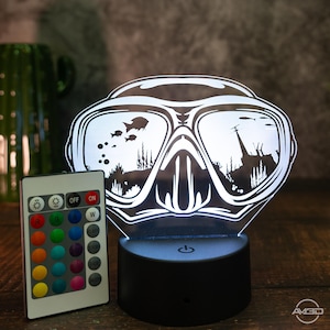 Könnte beinhalten: Ein weißes, 3D-gedrucktes Nachtlicht in Form einer Tauchermaske mit einer Fernbedienung zum Ändern der Lichtfarbe. Die Maske hat eine Silhouette von Fischen und Algen in den Gläsern.