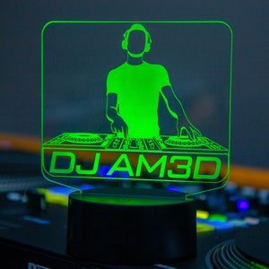 Könnte beinhalten: Grünes LED-Licht mit einer Silhouette eines DJs, der Musik auf einem Plattenspieler mischt. Das Licht zeigt "DJ AM3D".