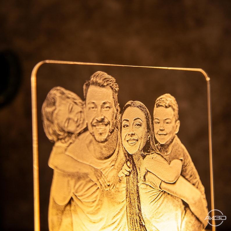 Peut inclure: Une lampe en acrylique grav&eacute;e sur mesure avec un portrait de famille d'un homme, d'une femme et de deux enfants. La lampe est &eacute;clair&eacute;e par derri&egrave;re, cr&eacute;ant une lueur chaleureuse.