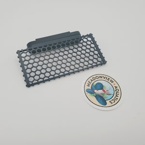 May include: Black plastic fish tank filter grate with a honeycomb design. The grate is attached to a black plastic frame.