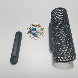 May include: Black plastic fish food holder with a hexagonal mesh design. The holder is attached to a wall mount. The holder is labeled "Meadowview Aquatics".