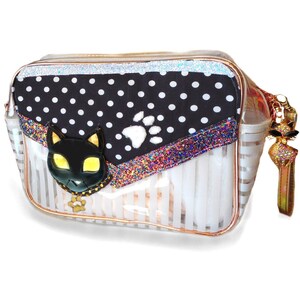 Puede incluir: Bolsa de cosméticos transparente a rayas con un diseño de cara de gato negro y huella de pata. La bolsa presenta una solapa de lunares blancos y negros con un ribete brillante. Un dije de gato dorado cuelga de la cremallera.