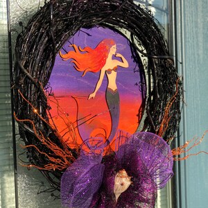 May include: A black twig wreath with a purple and orange mermaid illustration and a purple and silver mesh bow with a seashell.