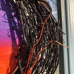 May include: A black twig wreath with red glitter accents. The wreath is made from natural twigs that have been painted black and then decorated with red glitter. The wreath is perfect for adding a touch of rustic elegance to your home decor.