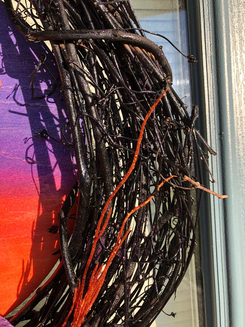 May include: A black twig wreath with red glitter accents. The wreath is made from natural twigs that have been painted black and then decorated with red glitter. The wreath is perfect for adding a touch of rustic elegance to your home decor.