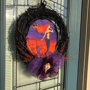 May include: A black twig wreath with a purple and silver mesh bow and a mermaid cutout on a purple, orange, and blue background.