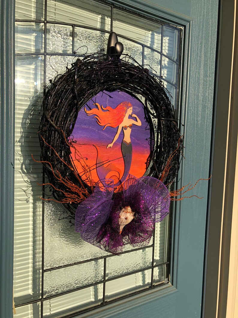 May include: A black twig wreath with a purple and silver mesh bow and a mermaid cutout on a purple, orange, and blue background.