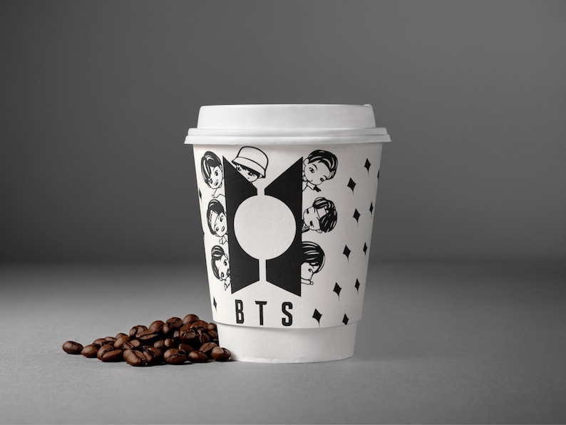 Pu&ograve; includere: Una tazza di caff&egrave; di carta bianca con un design in bianco e nero con facce di cartoni animati e le lettere "BTS". La tazza &egrave; piena di caff&egrave; e ha un coperchio bianco. Un piccolo mucchio di chicchi di caff&egrave; si trova accanto alla tazza.