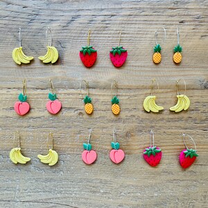 Può includere: Un set di 12 paia di orecchini a tema frutta. Gli orecchini sono realizzati in pasta polimerica e presentano una varietà di frutti, tra cui fragole, ananas, banane e pesche.