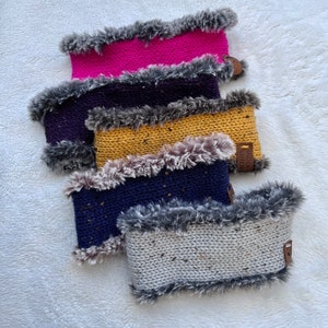 May include: Four knitted neck warmers with faux fur trim. The warmers are in pink, purple, yellow, and gray. The warmers have a label that says "Snug Stitch".