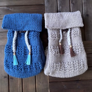 May include: Two knitted bags with a drawstring closure and tassels. One bag is blue and the other is beige.